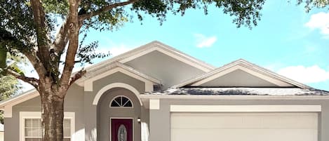 Une maison d’habitation avec un garage, une porte rouge et un arbre dans le jardin.
