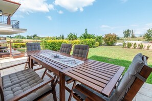 Eine Terrasse im Freien mit Holztisch und -stühlen, einer gepolsterten Bank sowie Blick auf einen gepflegten Garten und Rasen.