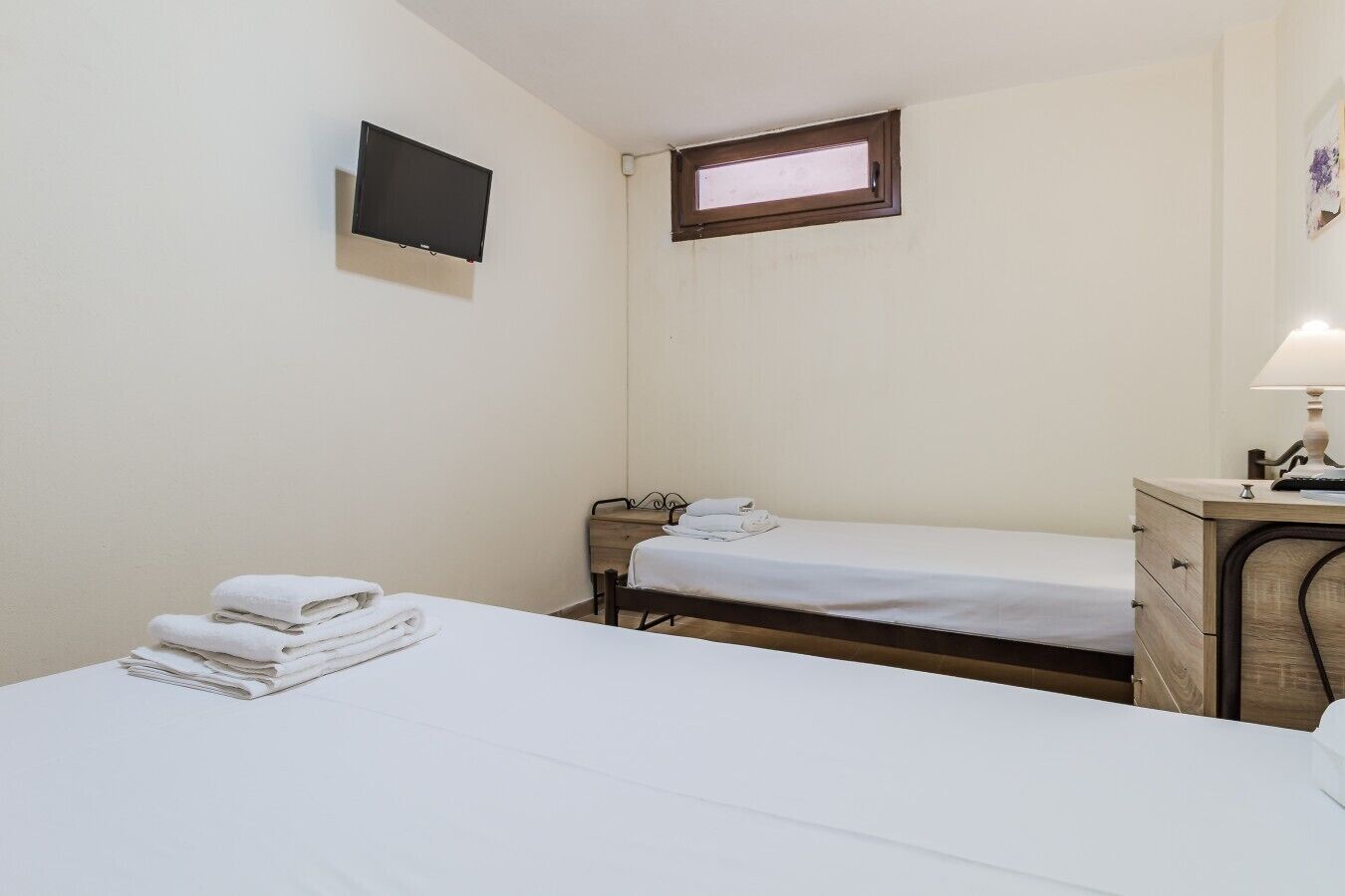 Ein Zimmer mit zwei Betten, einem Fernseher, einem Fenster und einem Schreibtisch mit Lampe.