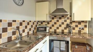 A kitchen with a stainless steel sink, a microwave, a stove, and a clock on the wall.
