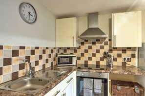 Una cocina con un lavamanos de acero inoxidable, microondas, estufa y un reloj en la pared.