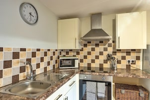 Una cocina con un lavamanos de acero inoxidable, microondas, estufa y un reloj en la pared.