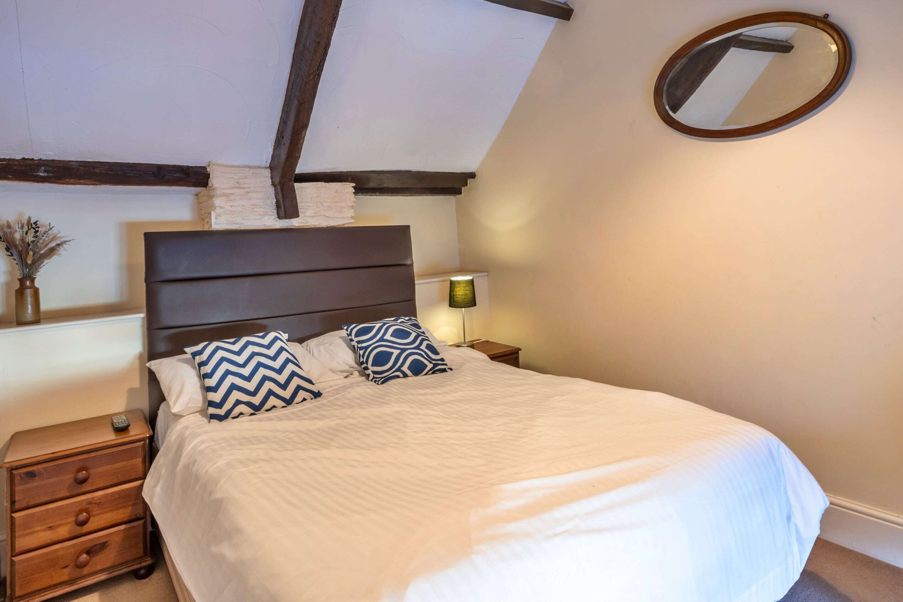A bedroom with a bed, a nightstand, a lamp, and a mirror on the wall.