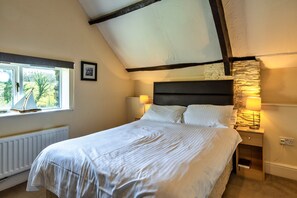 Un dormitorio con cama, ventana, un cuadro en la pared y una mesita de noche con lámpara.