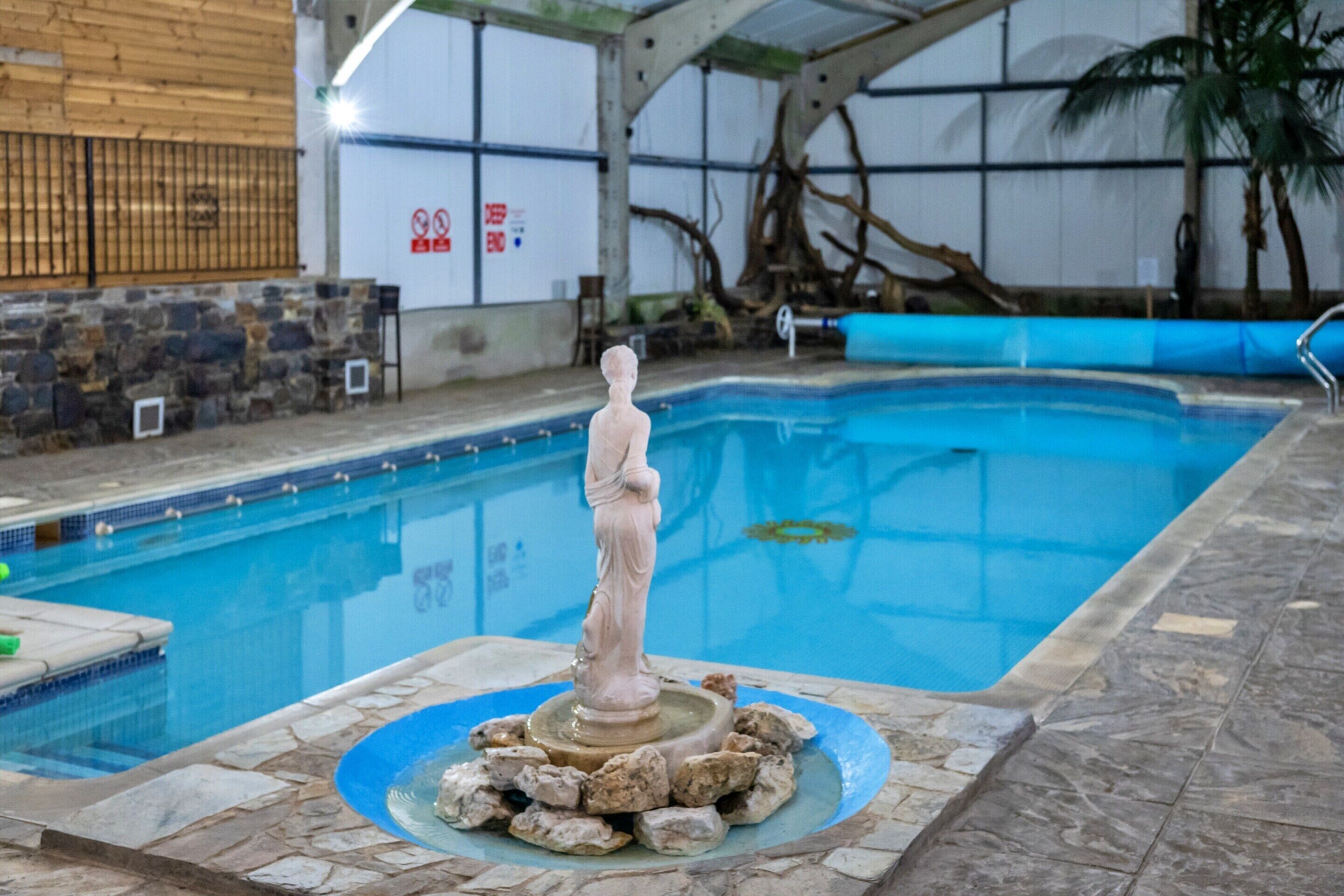 An indoor swimming pool with a statue in the center, surrounded by rocks.