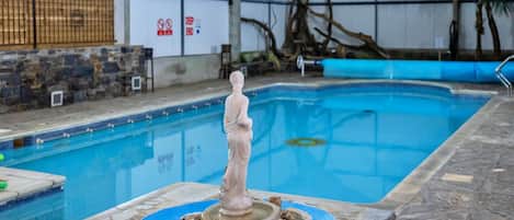 An indoor swimming pool with a statue in the center, surrounded by rocks.