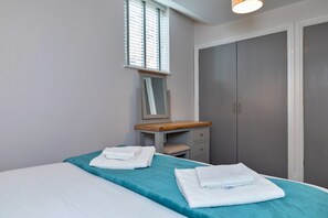 A bedroom with a bed, a bedside table, a mirror, a wardrobe, and a window with blinds. - Scenic Snowdonia Coastal Cabin (Ashbourne)