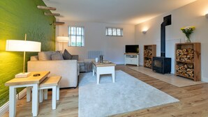A modern living room with a sofa, a coffee table, a TV, a fireplace, and a green accent wall. - Scenic Snowdonia Coastal Cabin (Ashbourne)