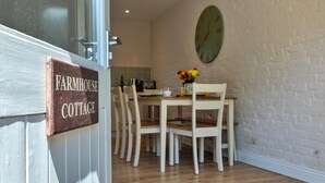 A dining area with a wooden table and chairs, a clock on the wall, and a sign reading 'Farmhouse Cottage.' - Scenic Snowdonia Coastal Cabin (Ashbourne)