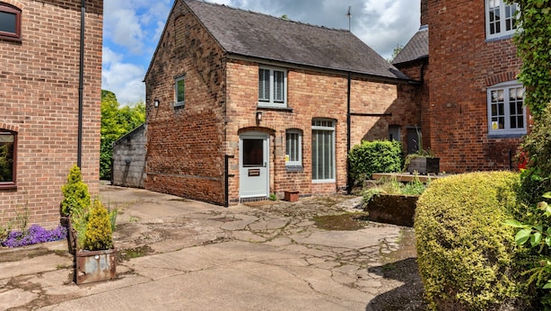 A brick farmhouse with a white door, a small garden, and a paved courtyard. - Scenic Snowdonia Coastal Cabin (Ashbourne)