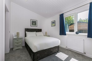 A bedroom with a bed, bedside tables, a window with curtains, and a radiator. - Scenic Perthshire Chalet With Sauna (Perth)