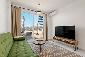 A modern living room with a green sofa, a flat-screen TV, and a large sliding glass door leading to an outdoor terrace. - Apartment with Terrace and Rooftop in Casares Costa (Casares)