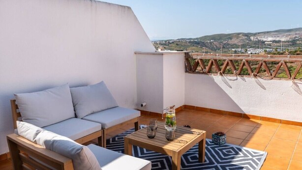 En terrasse med en sofa, et bord og udsigt over et bakket landskab.