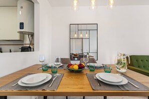 A dining area with a wooden table set for four, surrounded by chairs. A fruit bowl is on the table, and there are glasses and cutlery. - Apartment with Terrace and Rooftop in Casares Costa (Casares)