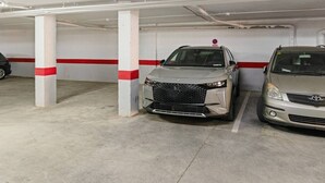 En parkeringskælder med to biler parkeret under hvide søjler med røde striber.