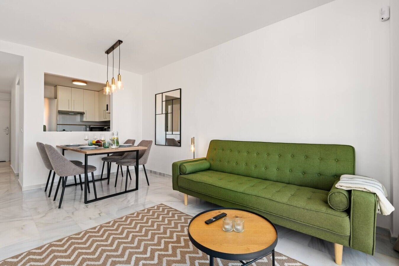 Ein modernes Wohnzimmer mit einem grünen Sofa, einem Essbereich mit Tisch und Stühlen sowie einer Küche im Hintergrund.