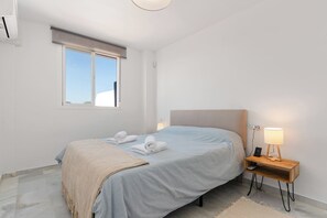 Een slaapkamer met een bed, een nachtkastje met lamp, een raam en een airconditioning.