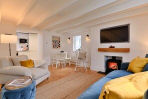 A living room with a sofa, a coffee table, a fireplace, and a television mounted on the wall. - Refined Cornish Heritage Cottage for 3 (Penzance)