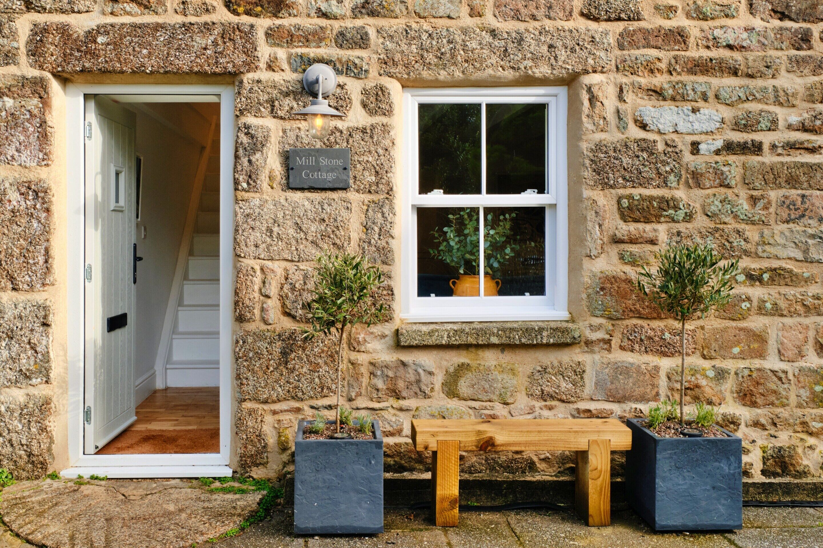 A stone cottage with a wooden bench, a door, and a window with a potted plant.