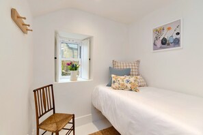 A bedroom with a single bed, a window with a view of greenery, a wooden chair, and a framed picture on the wall. - Refined Cornish Heritage Cottage for 3 (Penzance)