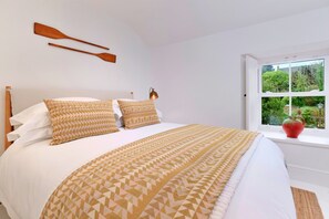A bedroom with a bed, pillows, a window, and a view of greenery outside. - Refined Cornish Heritage Cottage for 3 (Penzance)