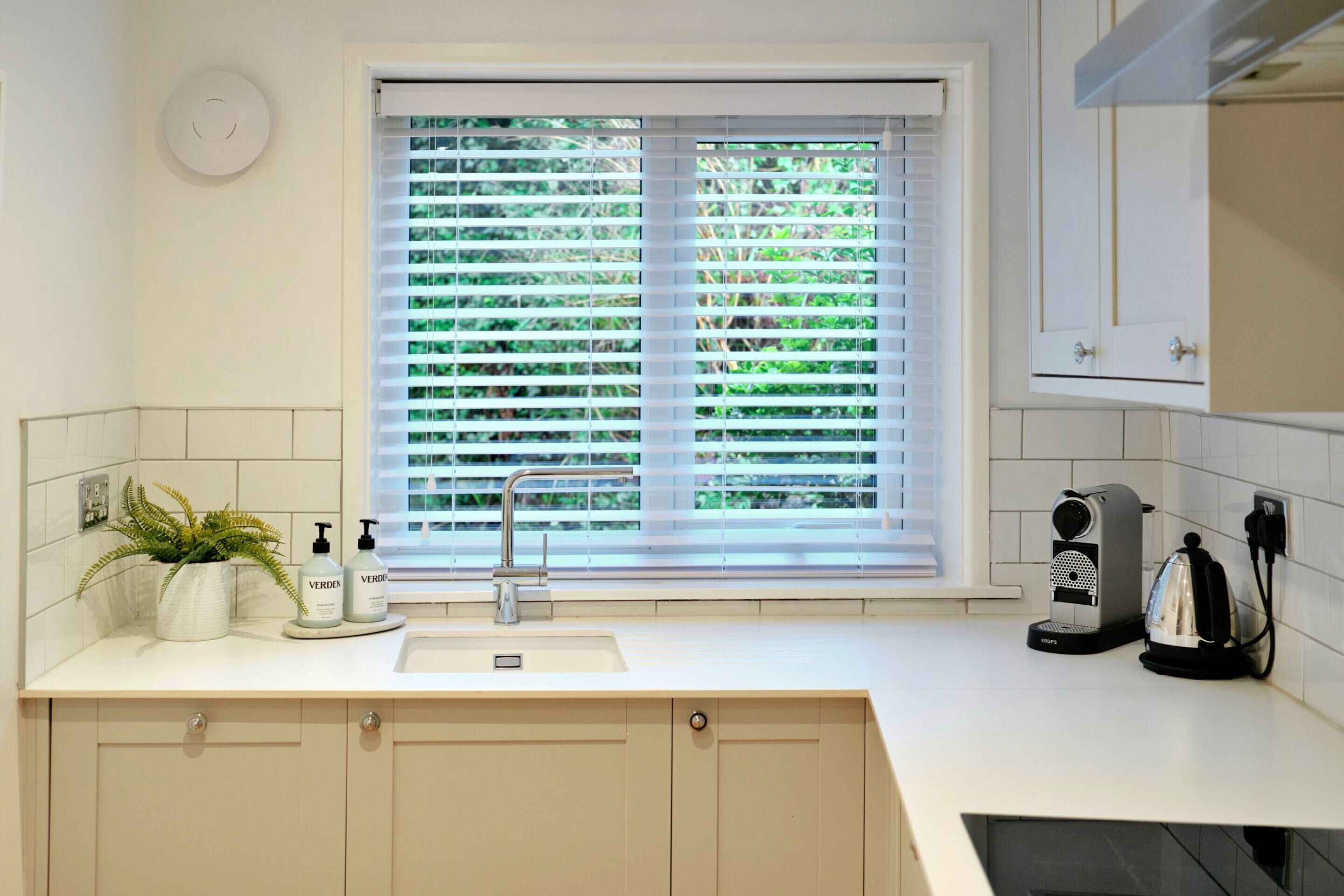 Eine Küche mit Fenster, Spüle, Wasserhahn, einer Pflanze und einem Wasserkocher.
