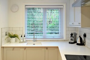 A kitchen with a window, a sink, a faucet, a plant, and a kettle. - Refined Cornish Heritage Cottage for 3 (Penzance)