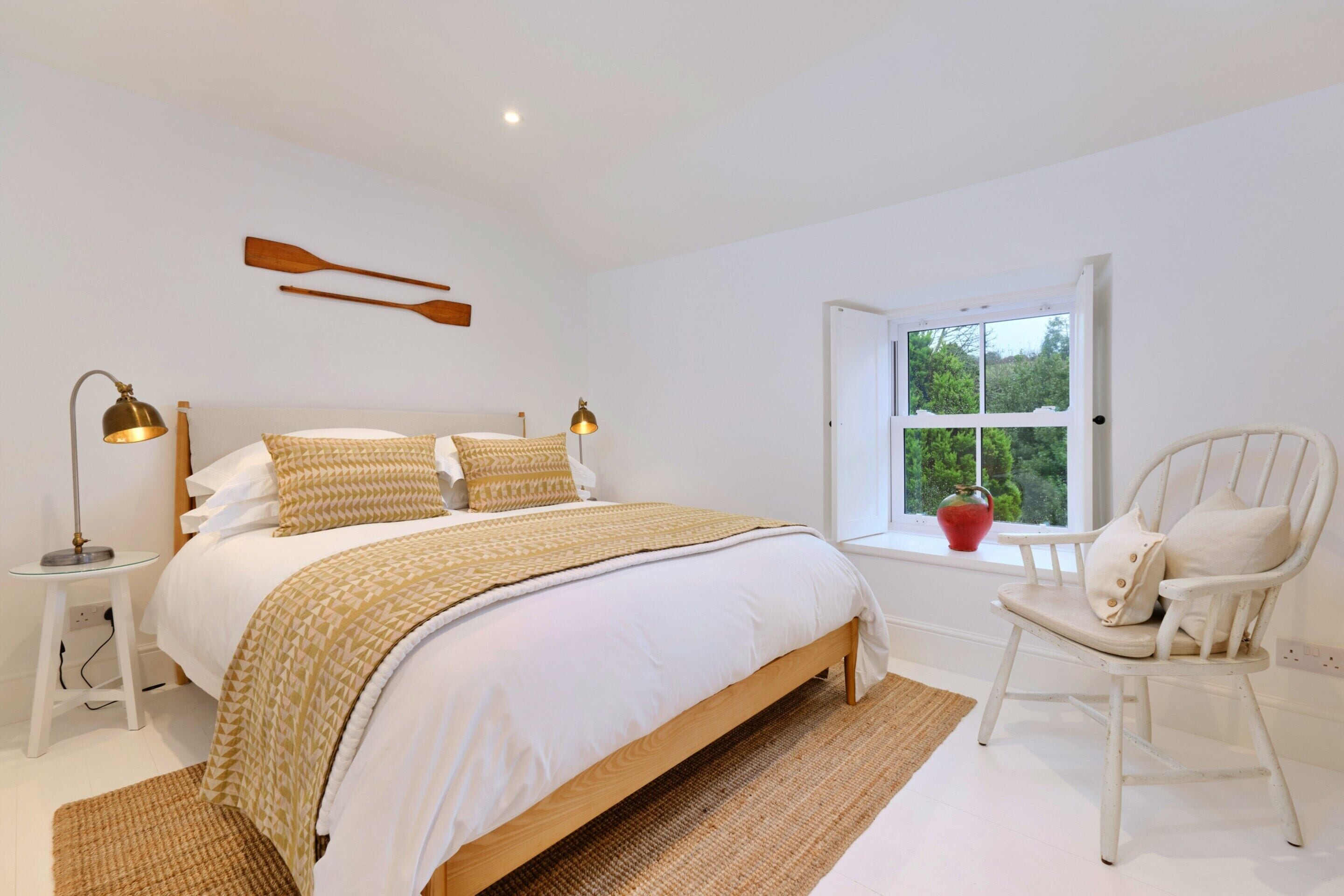 A bedroom with a large bed, two bedside lamps, a window with a view, and a chair.