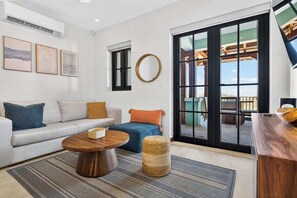 A modern living room with a sofa, coffee table, and ottoman, a large window with a view, and a wooden accent wall. - Las Catalinas Escape, Ocean View & Plunge Pool (Las Catalinas)