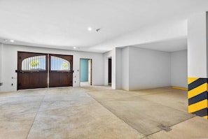 A spacious garage with a concrete floor, a large wooden garage door, and a blue door leading to another room. - Las Catalinas Escape, Ocean View & Plunge Pool (Las Catalinas)