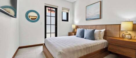 A bedroom with a wooden bed, bedside tables, a wall-mounted mirror, a door, and a painting.
