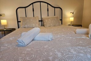 Ein ordentlich bezogenes Bett mit einem gemusterten Überwurf, zwei Kissen und aufgerollten Handtüchern.