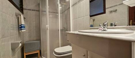 Un baño moderno con cabina de ducha, inodoro y tocador con lavabo.