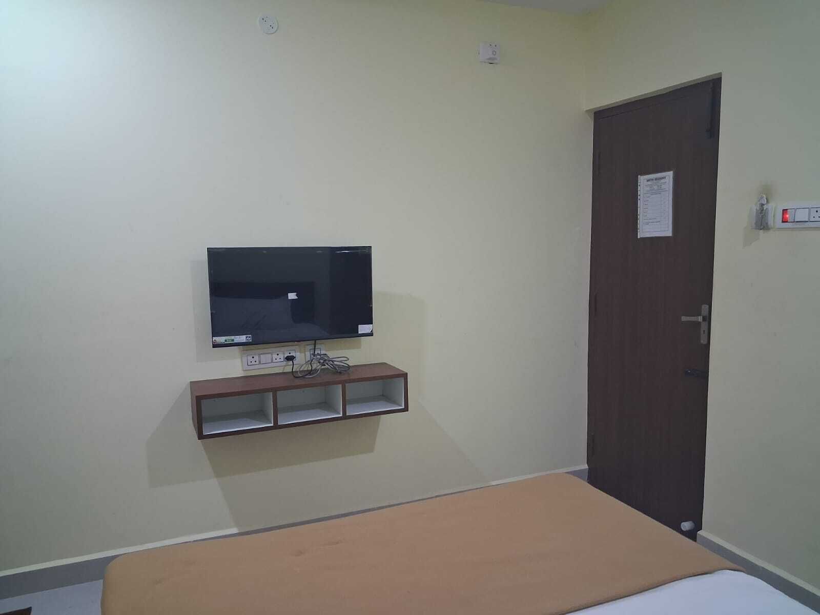 Una habitación con una cama, un televisor fijado a la pared, una puerta con un aviso y enchufes.