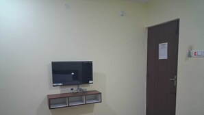 Una habitación con una cama, un televisor fijado a la pared, una puerta con un aviso y enchufes.