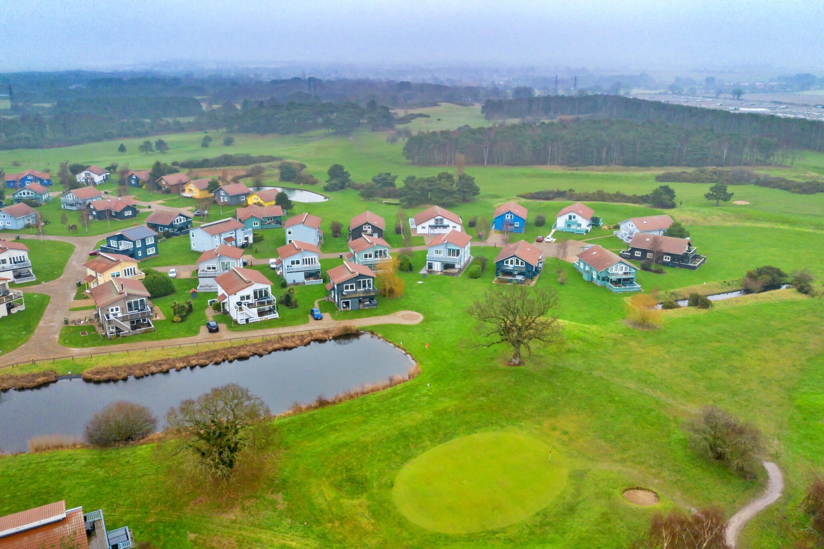 Um bairro residencial com casas, um lago e um campo de golfe ao fundo.