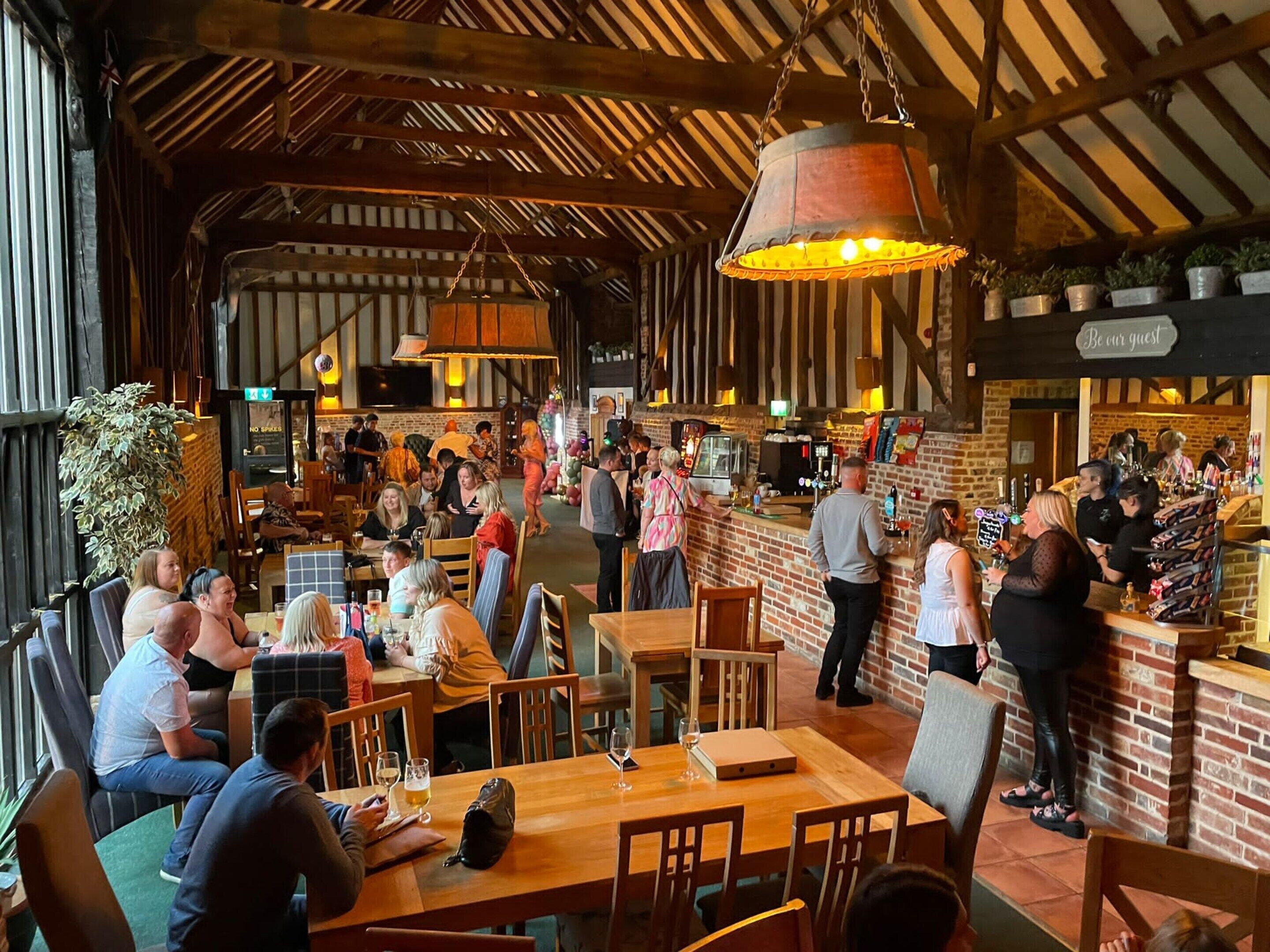 A bustling restaurant with wooden tables and chairs, a bar area, and a hanging light fixture.
