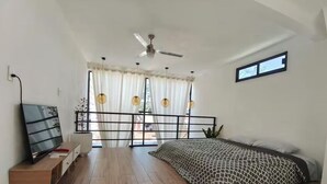 Ein Schlafzimmer mit einem Bett, einem Fernseher, einem Deckenventilator und einem Fenster mit Vorhängen.
