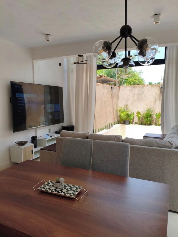 A modern living room with a flat-screen TV, a dining table with a decorative tray, and a sofa.