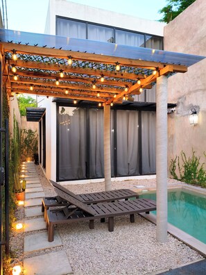 A covered outdoor seating area with string lights, a pool, and a pathway leading to a building. - Casa Jungla, the perfect place to connect with nature. (Palenque)
