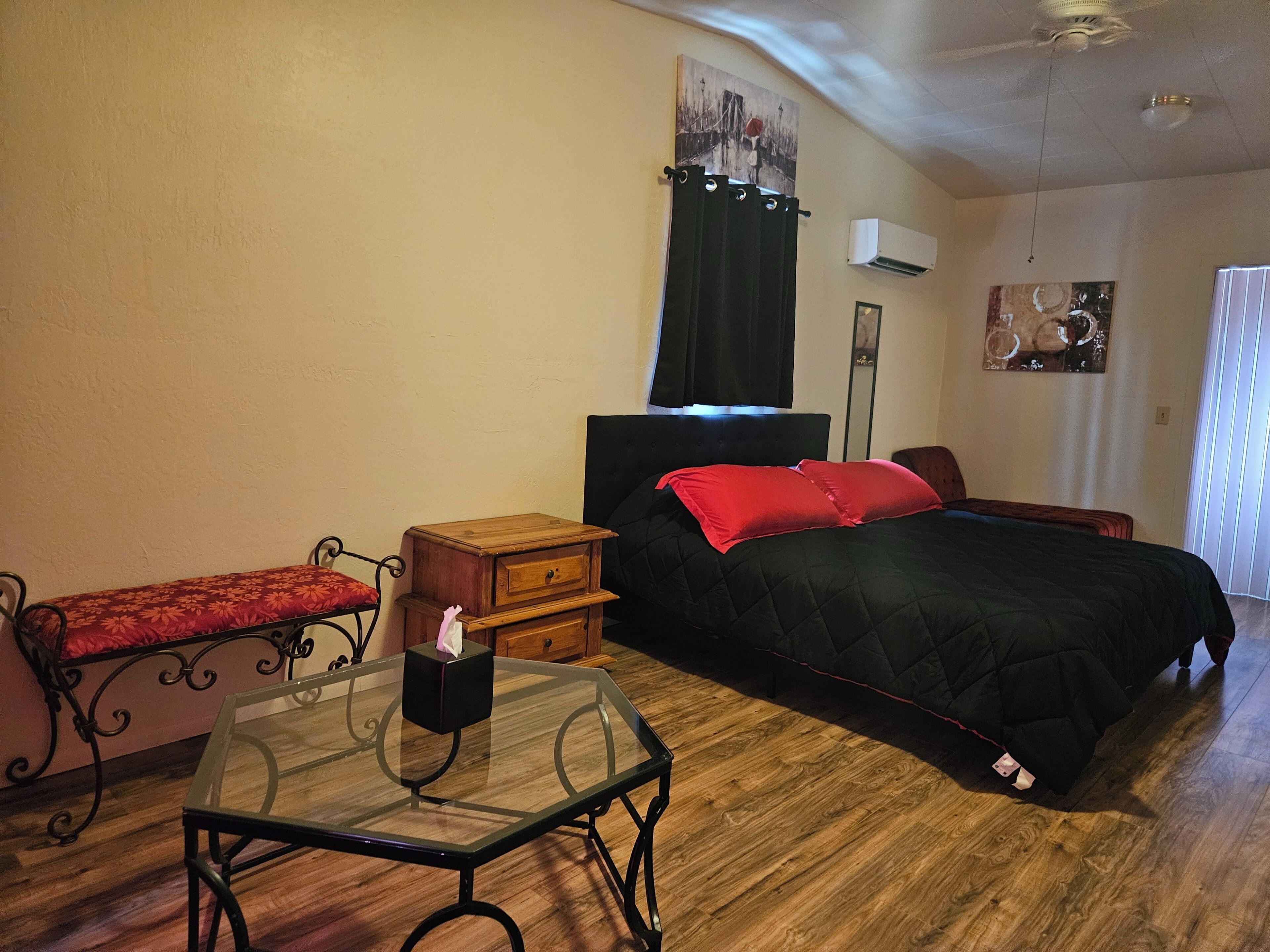A bedroom with a bed, bedside table, nightstand, and a window with curtains.