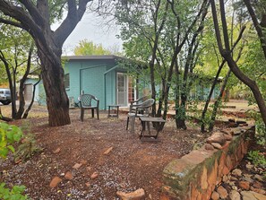 Un espacio de descanso rústico al aire libre con un cobertizo pequeño, rodeado de árboles y suelo de grava.