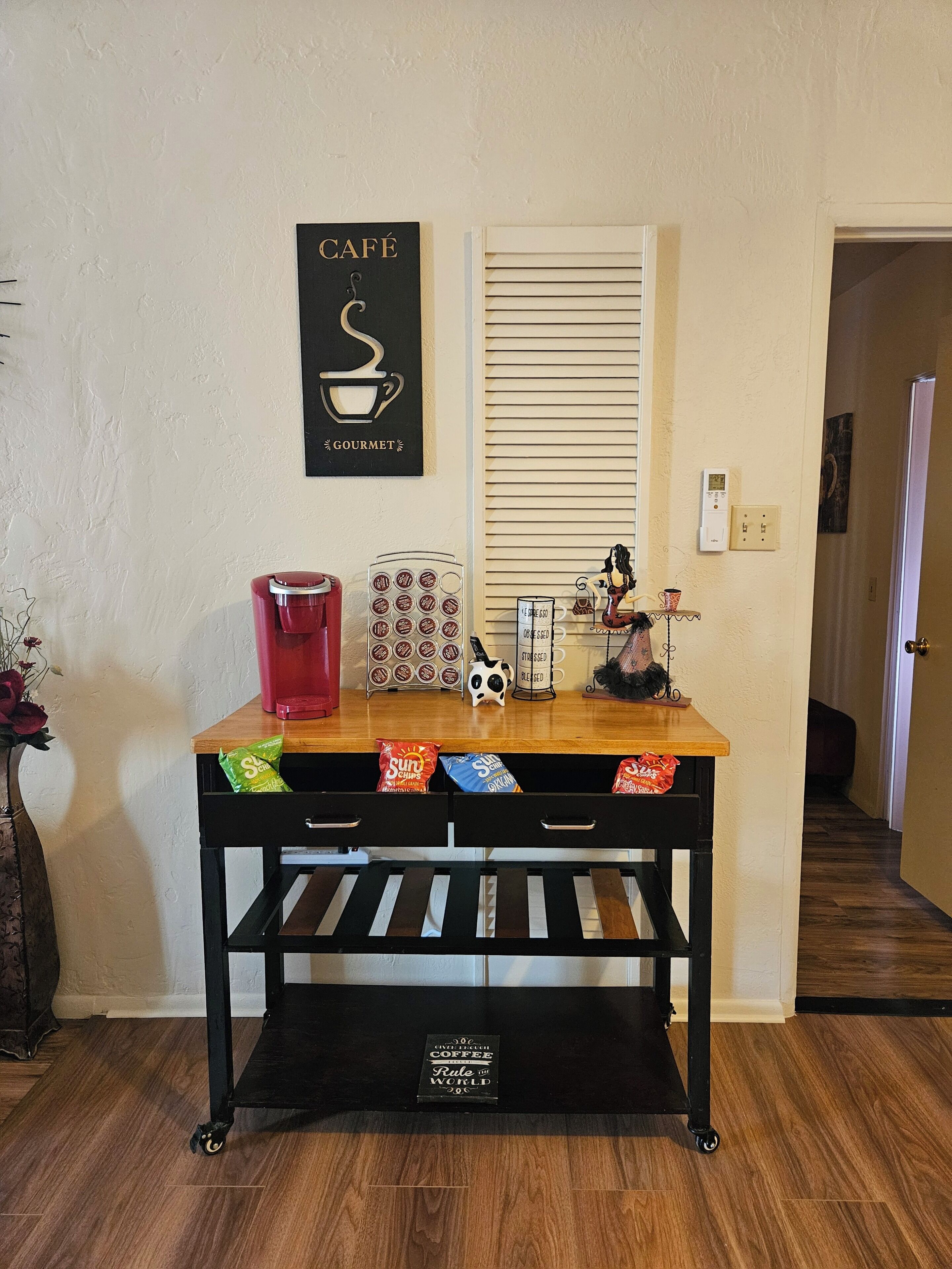 A coffee station with a sign reading 'CAFE GOURMET,' a coffee machine, a coffee grinder, and a bag of coffee pods.