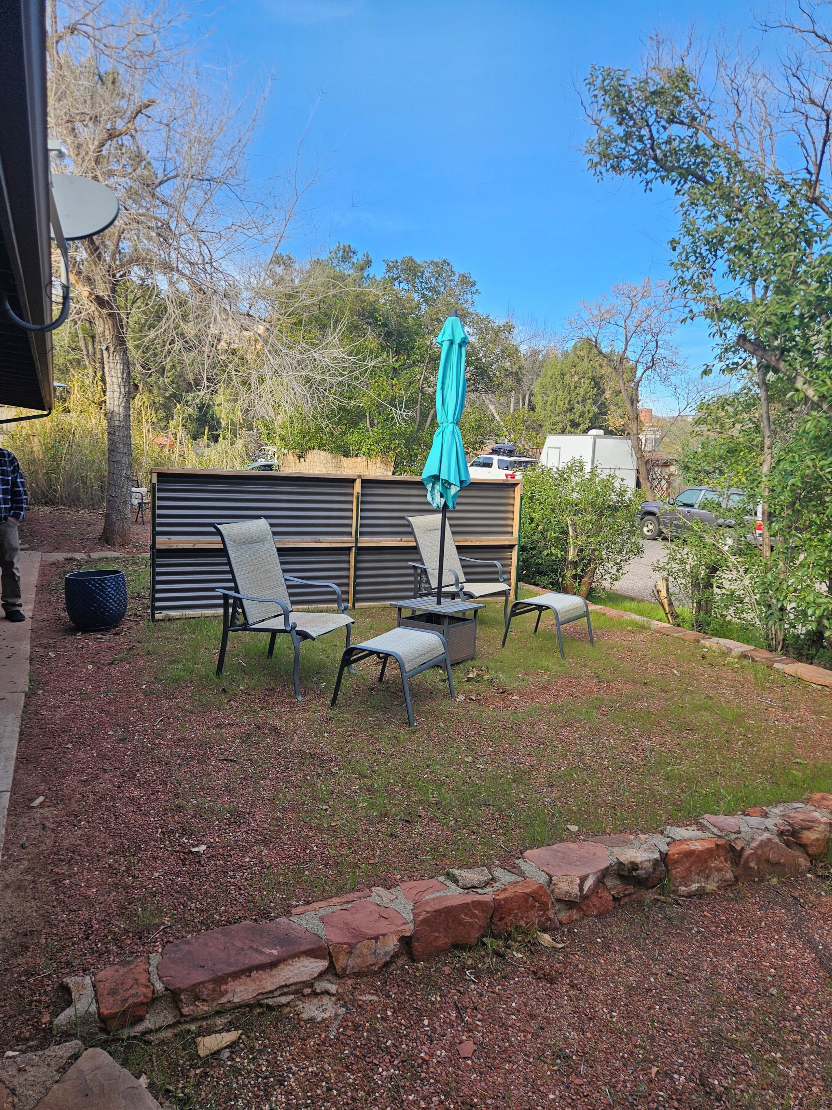 Un espace extérieur aménagé avec une table et des chaises, un parasol vert et une bordure en briques.