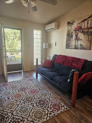 A room with a sofa, a patterned rug, a painting on the wall, and an air conditioning unit.