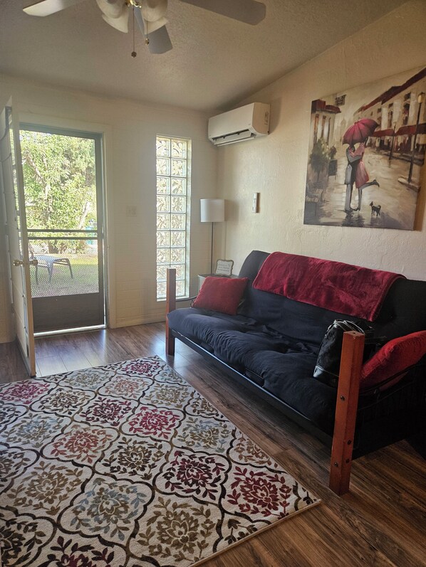 A room with a sofa, a patterned rug, a painting on the wall, and an air conditioning unit.