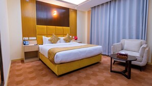 Habitación de hotel con una cama grande, una mesita de noche con lámpara, una silla y una pequeña mesa con una caja.