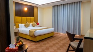 Habitación de hotel con una cama grande, una mesita de noche con frutero, una silla y un escritorio.