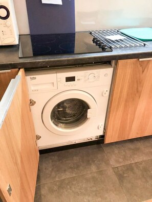 A compact washing machine with a control panel, situated in a small laundry area with a countertop above. - Apartment in Avoriaz, MALINKA residence, La Falaise residential neighborhood (Plouzané)