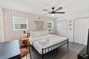 Ein Schlafzimmer mit einem Bett, einem Deckenventilator, einem an der Wand befestigten Schild, einem Schreibtisch und einem Stuhl.